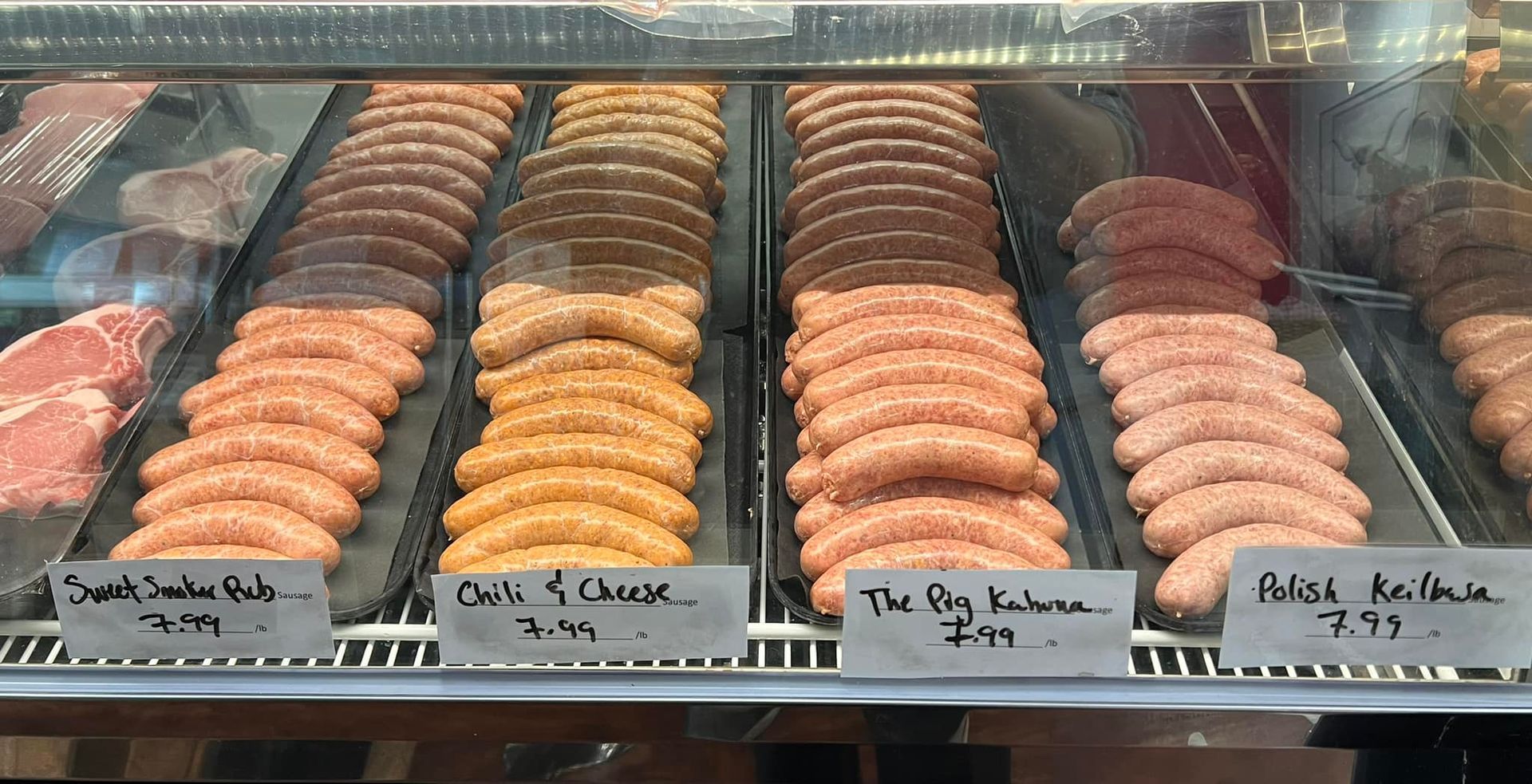 Display case with rows of sausages, including smoked, chili cheese, and others, with price tags.