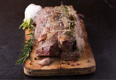 Roast beef tied with twine, rosemary, and garlic on a wooden board.