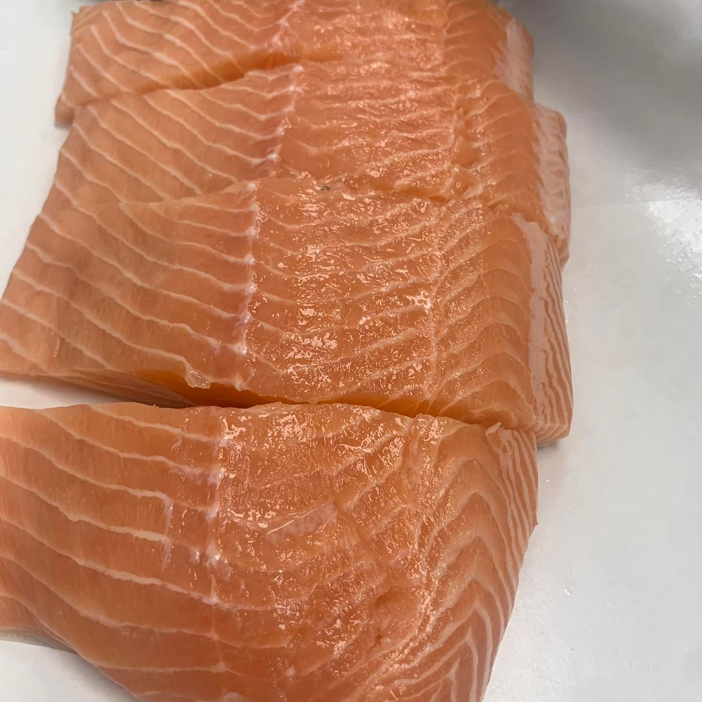 Four raw salmon fillets on a white surface, showing orange flesh and white fat lines.
