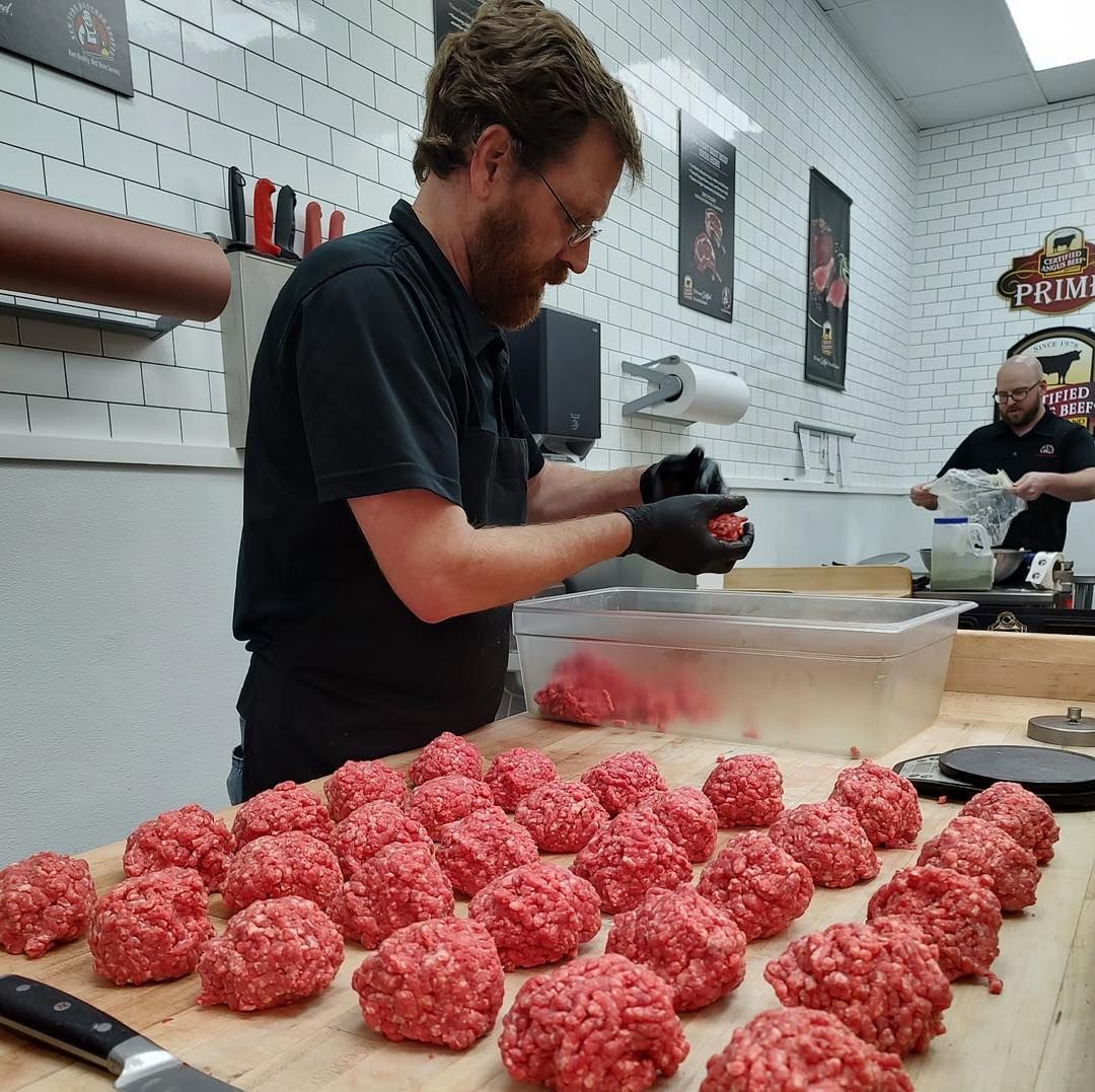 A man forms ground meat into patties on a wooden counter in a butcher shop.