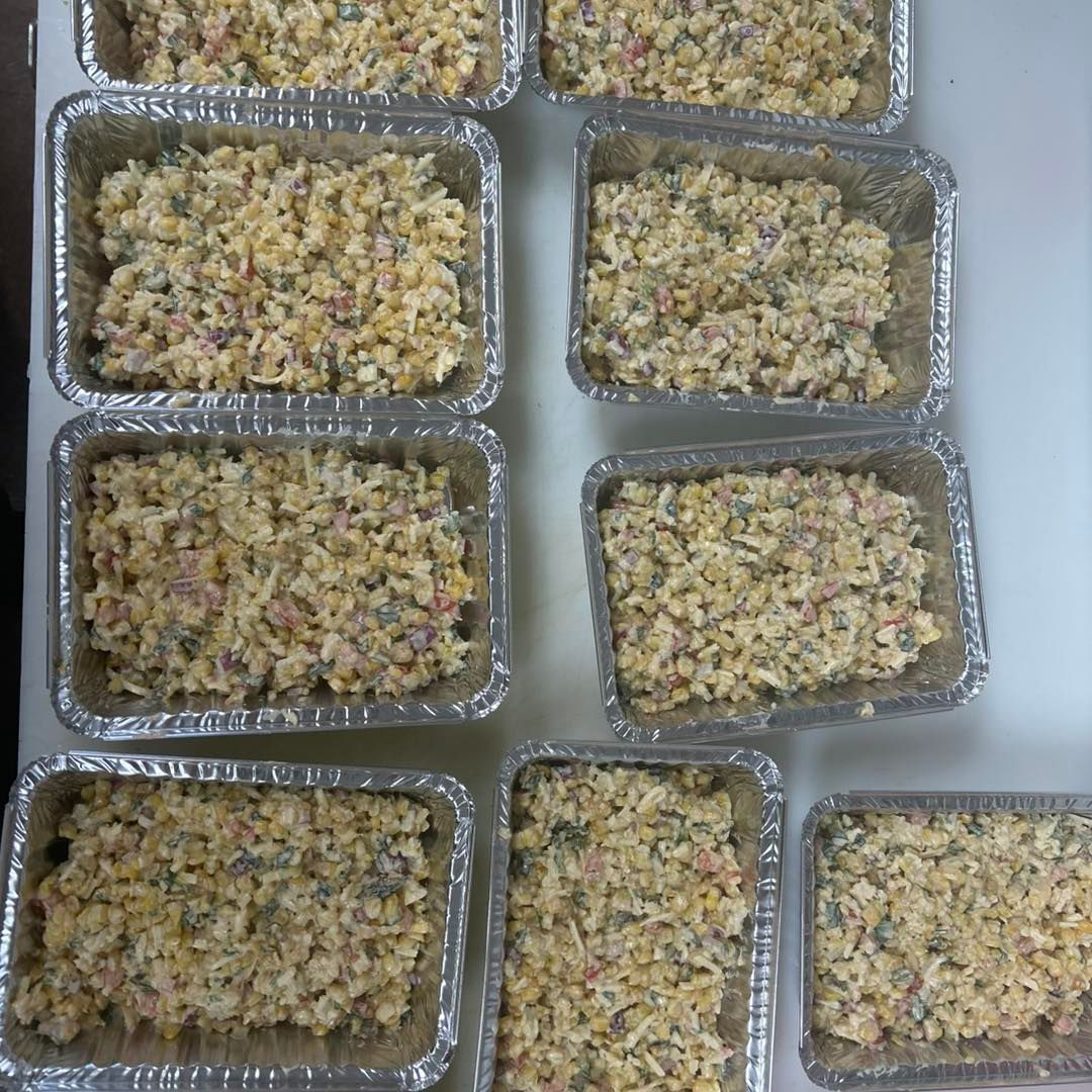 Aluminum foil containers filled with a yellow food mixture, likely a casserole or salad, prepared for individual servings.