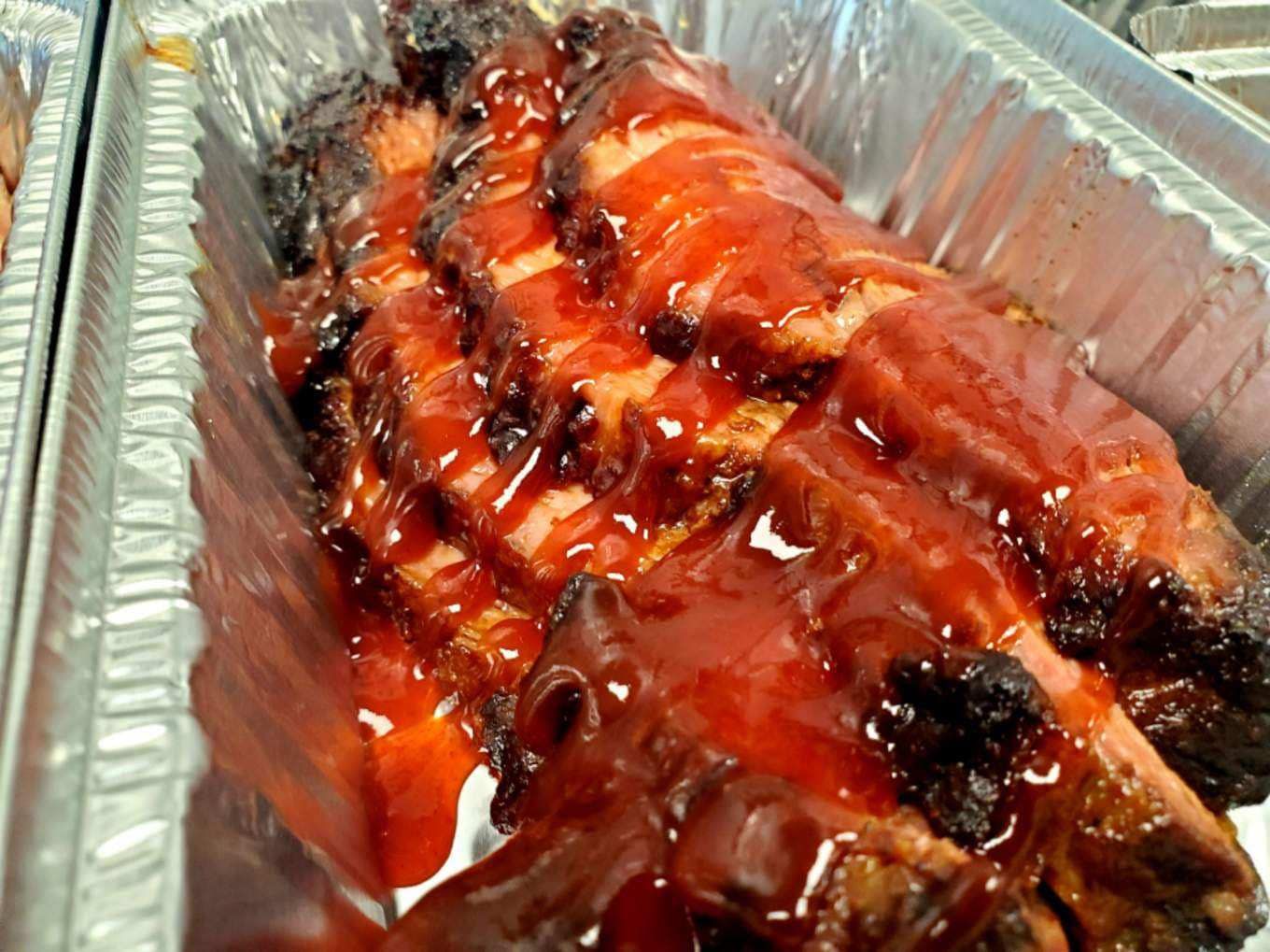 Sliced BBQ brisket in a foil pan, drizzled with red sauce.