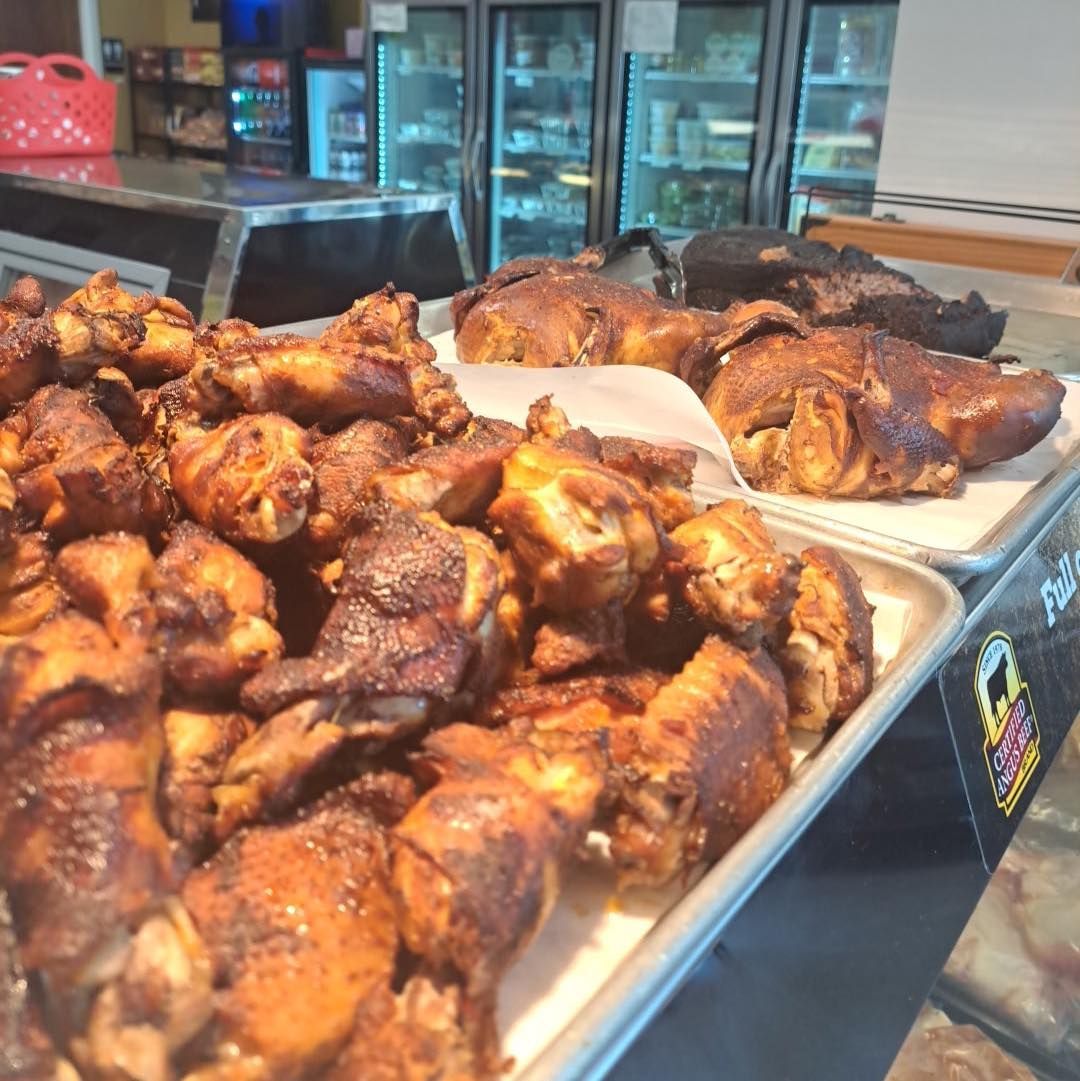 Smoked chicken pieces and whole chickens displayed on trays behind a deli counter.