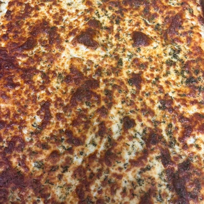 Close-up of a cheesy pizza with herbs sprinkled on top, with golden-brown and white textures.