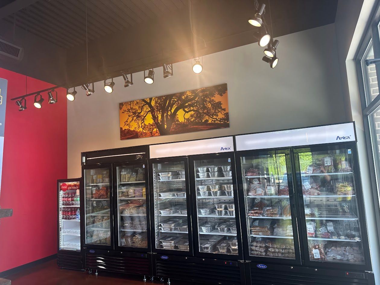 Refrigerated food display in a store, with a painting and track lighting above.