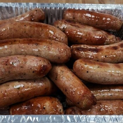 Cooked sausages piled in a foil container, with a glossy, brown exterior.