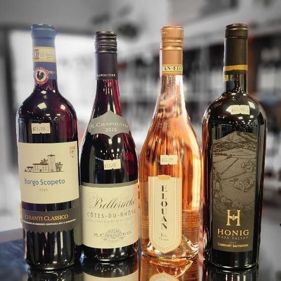 Four wine bottles: red, rosé, and two different dark reds, on a surface in a store.