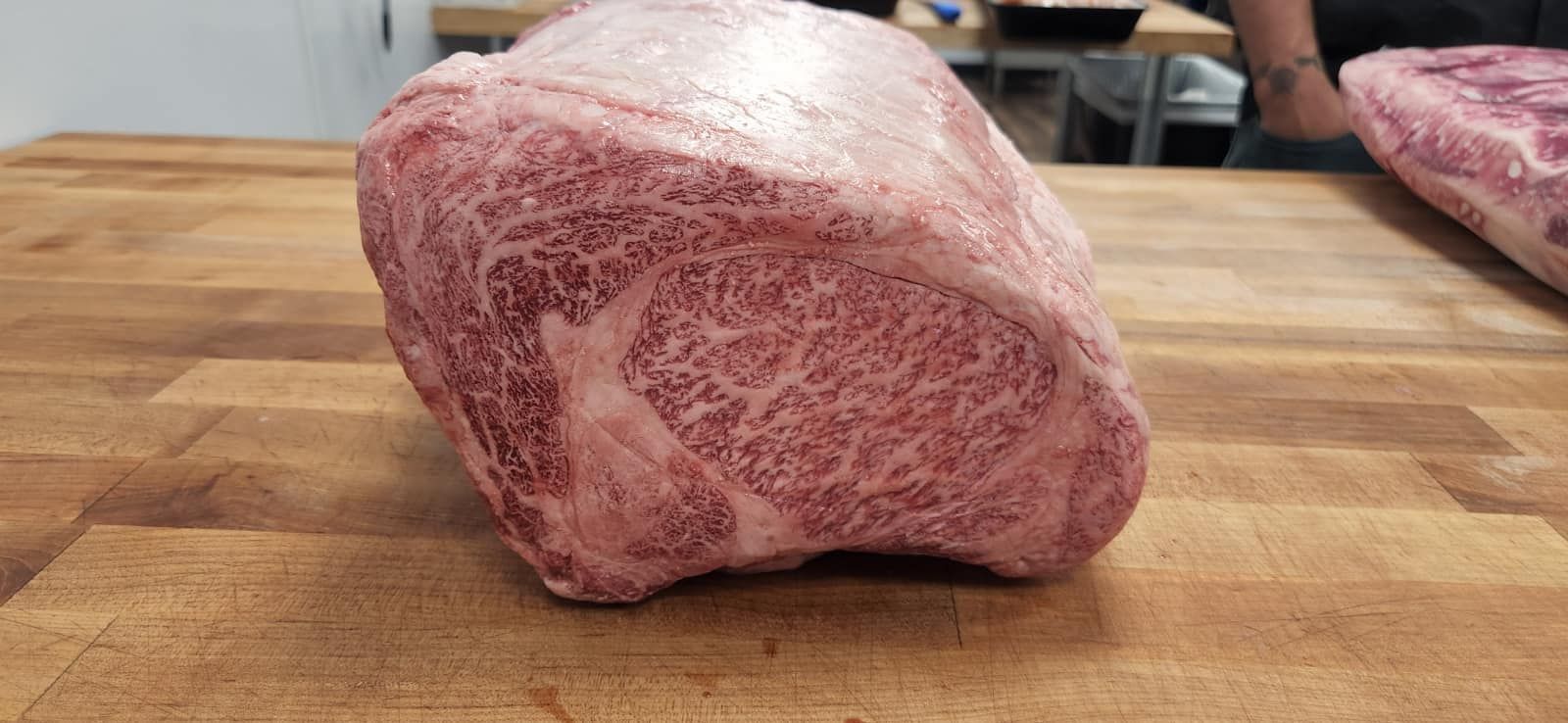 Close-up of a large raw cut of Wagyu beef with intense marbling, resting on a wooden surface.