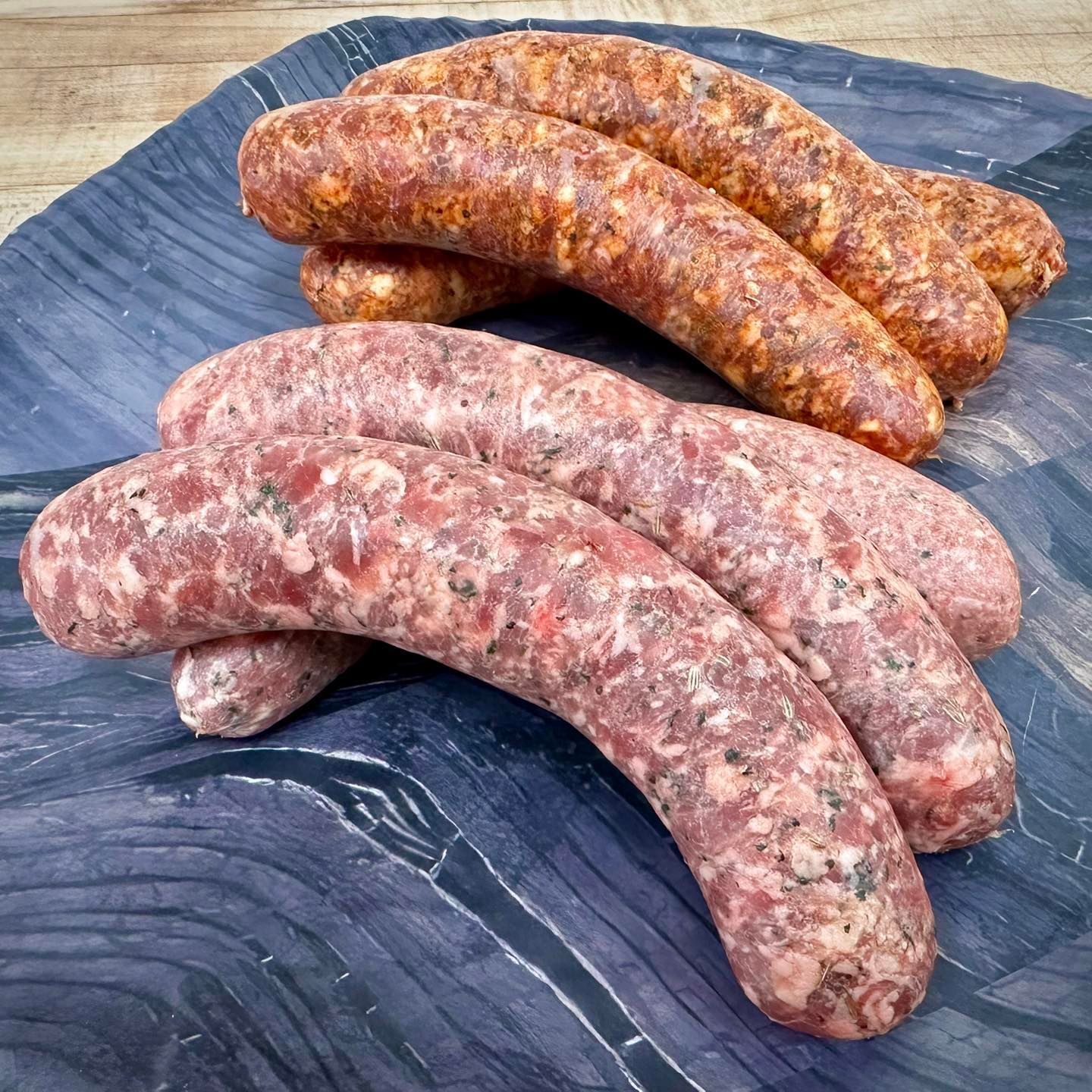 Sausages, two varieties, on a dark surface. One is light pink, the other is reddish-brown.