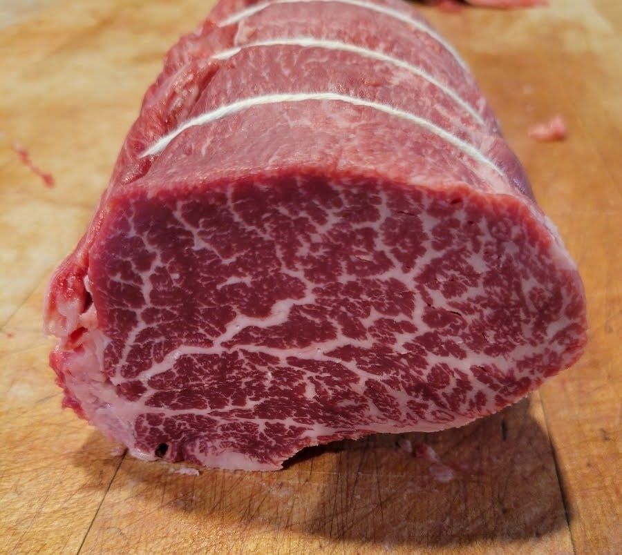 Close-up of a tied, raw beef roast with visible marbling, resting on a wooden surface.