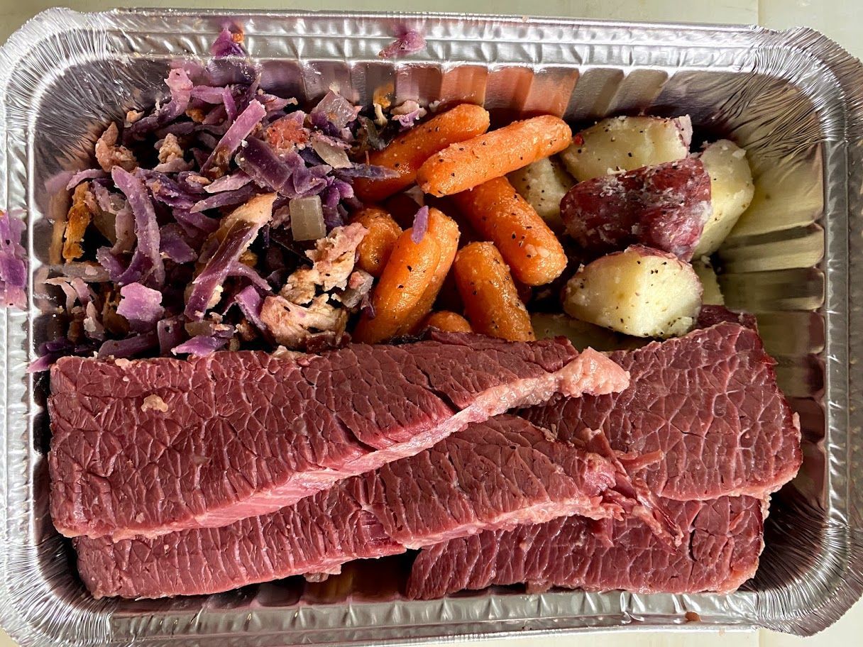 Meal in a foil container: sliced corned beef, red cabbage, carrots, and potatoes.