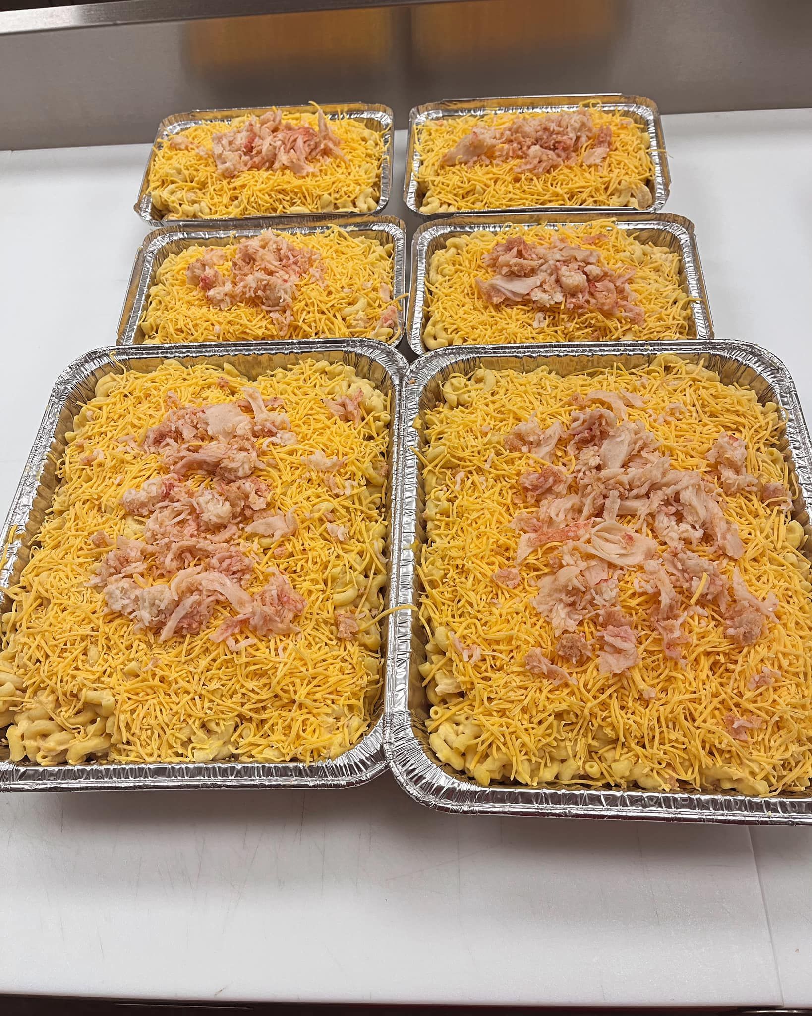 Six trays of mac and cheese, topped with shredded cheese and diced meat.