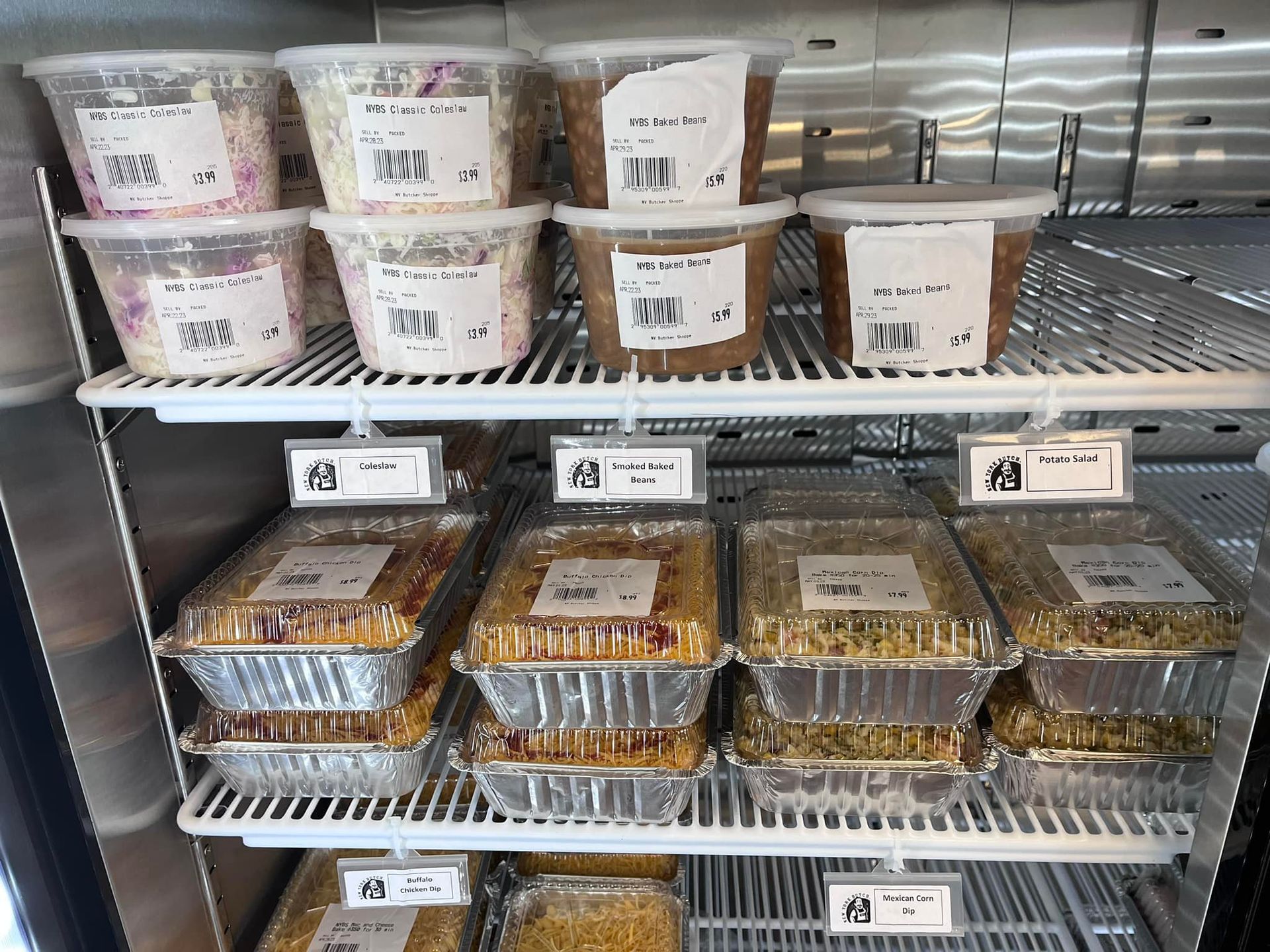 Shelves of prepared food containers in a refrigerator, including salads and entrees.