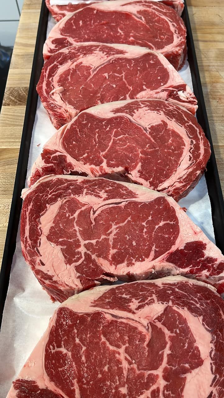 Five raw, red ribeye steaks with visible marbling sit in a tray.