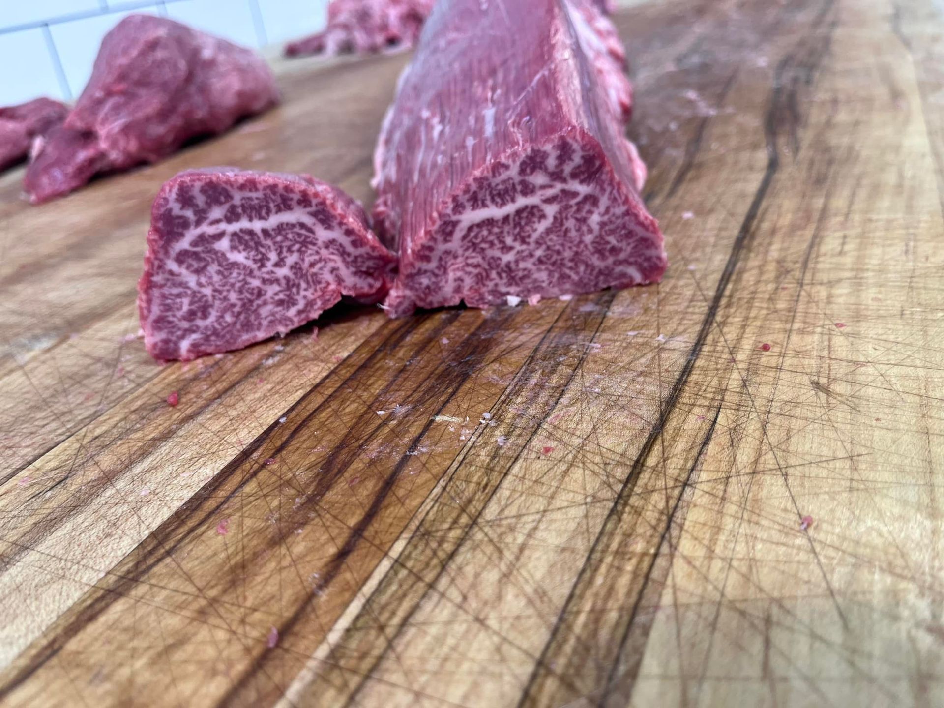 Close-up of a raw, marbled beef cut on a worn wooden cutting board.
