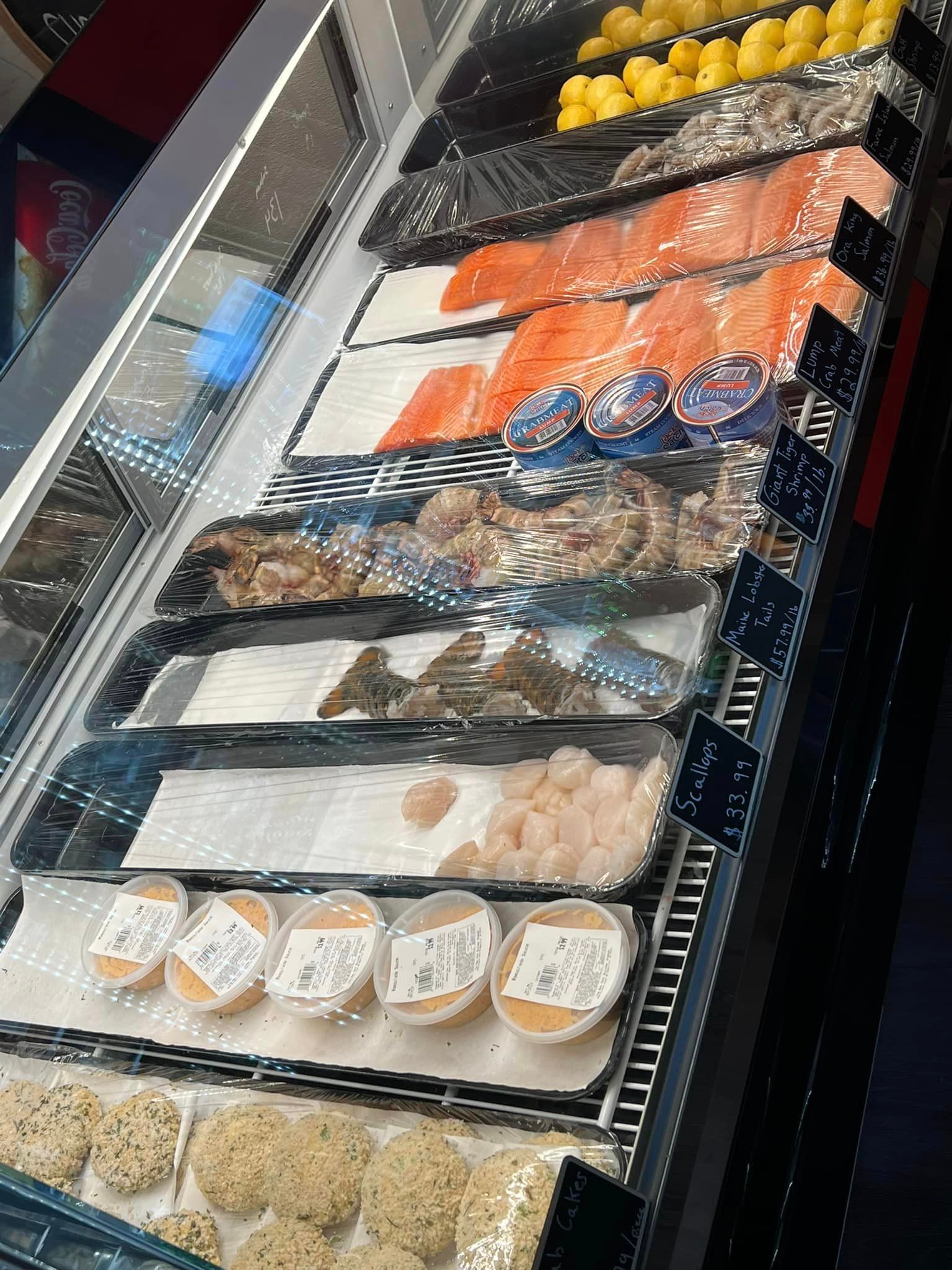 Display case with various seafood products: salmon, scallops, and fish cakes.