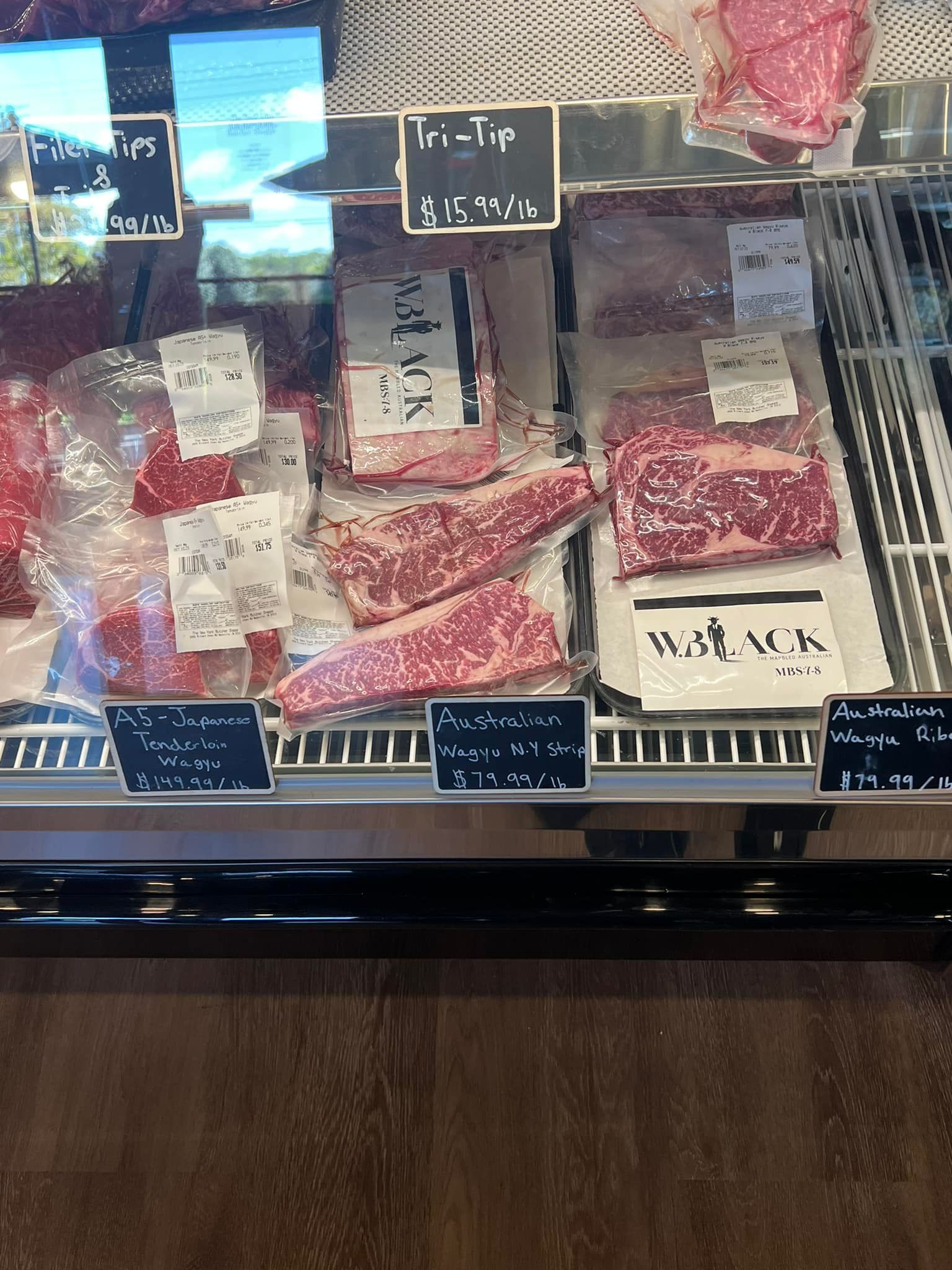 Display case with various cuts of raw beef, including steaks, with price tags.
