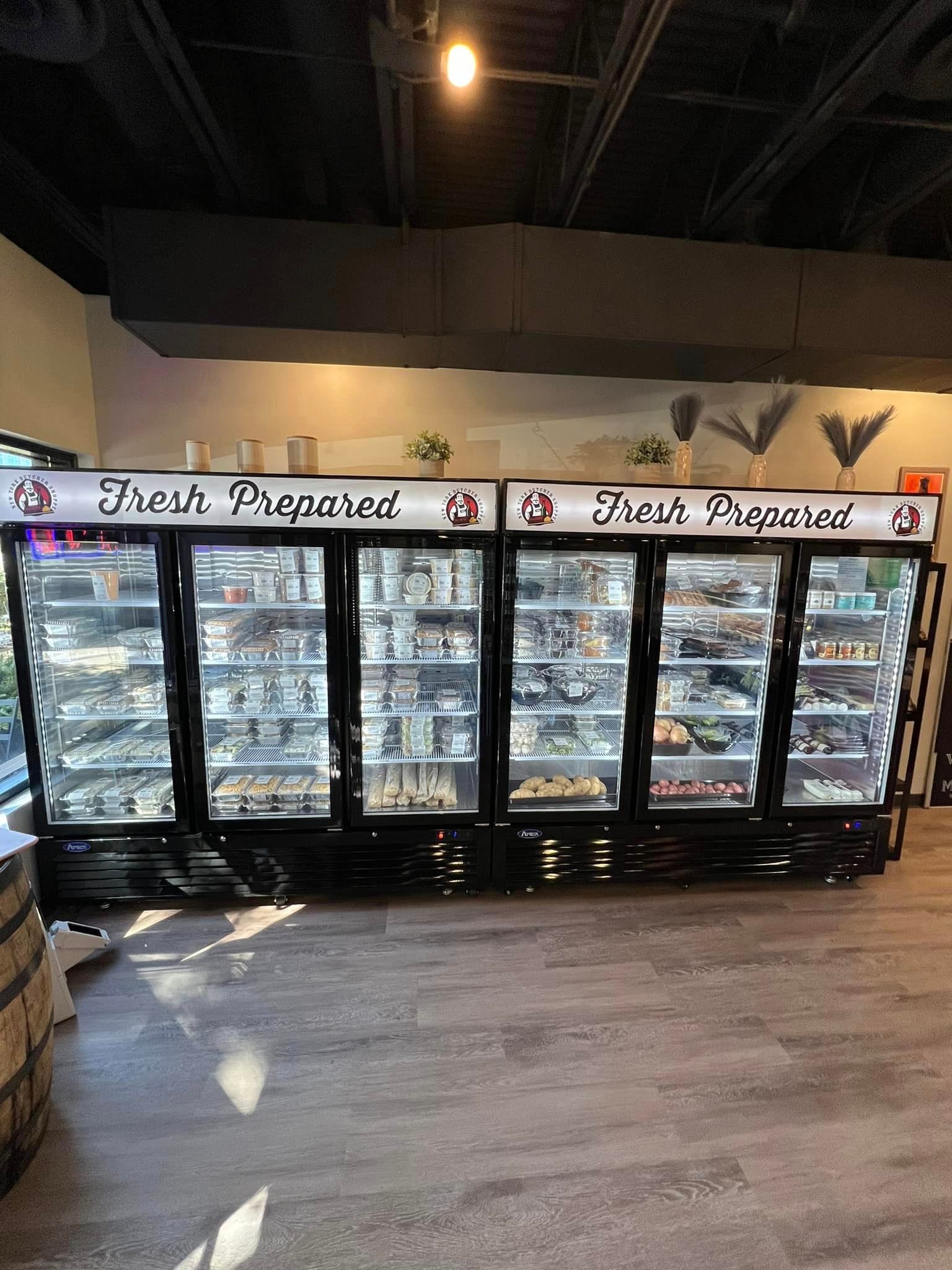 Refrigerated display cases in a store stocked with prepared food items, black frames, and a light above.