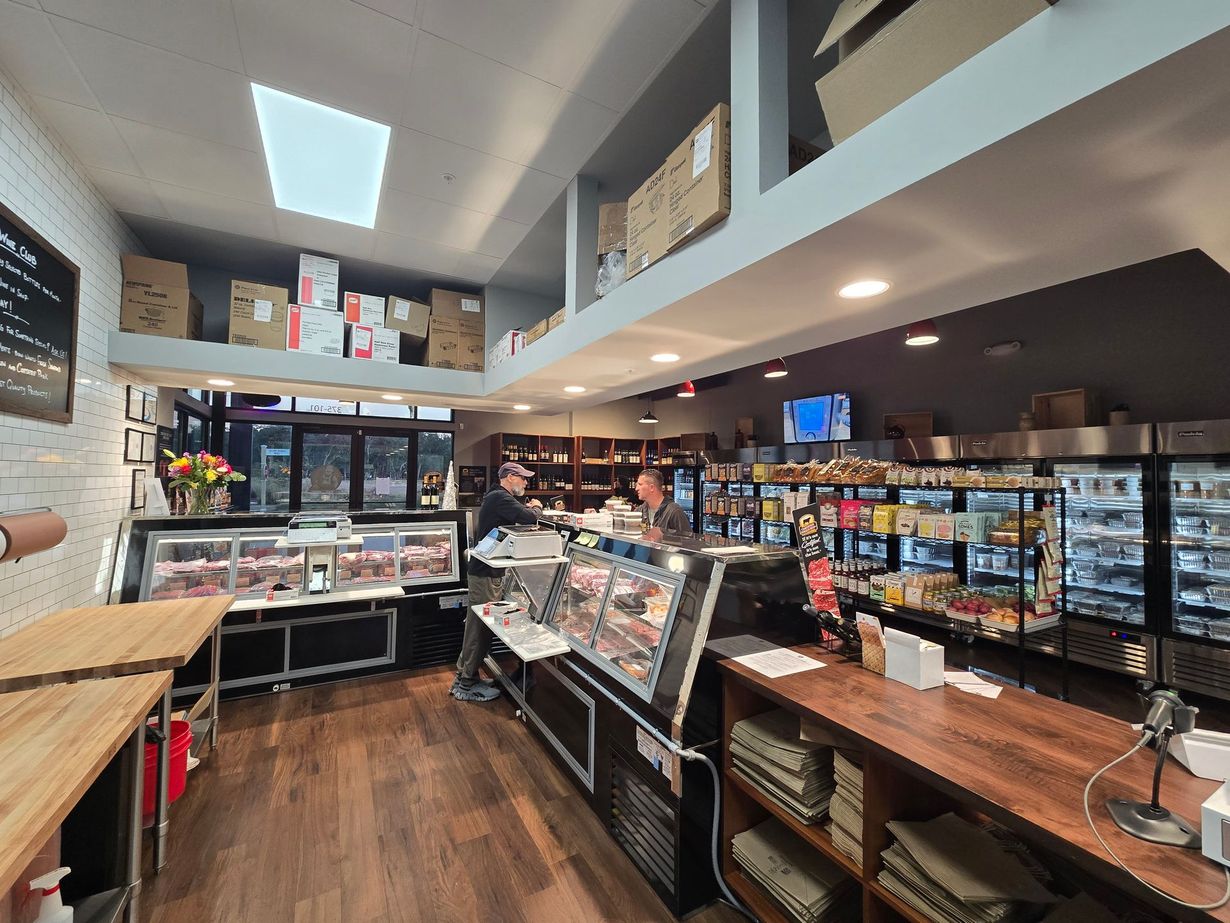 Interior of a deli with two employees, display cases of food, and overhead storage.