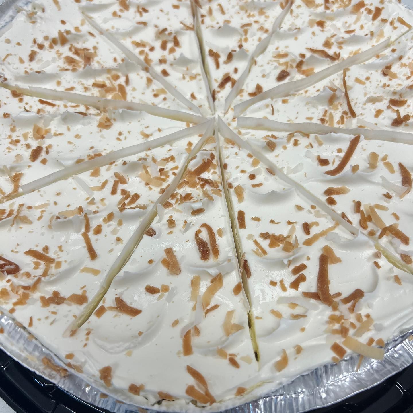 Coconut cream pie with whipped topping and toasted coconut flakes, sliced into pieces.