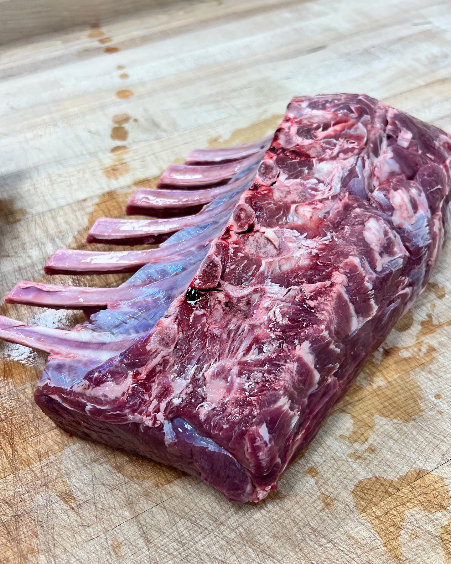 Rack of raw lamb on a wooden cutting board, showing ribs, red meat.
