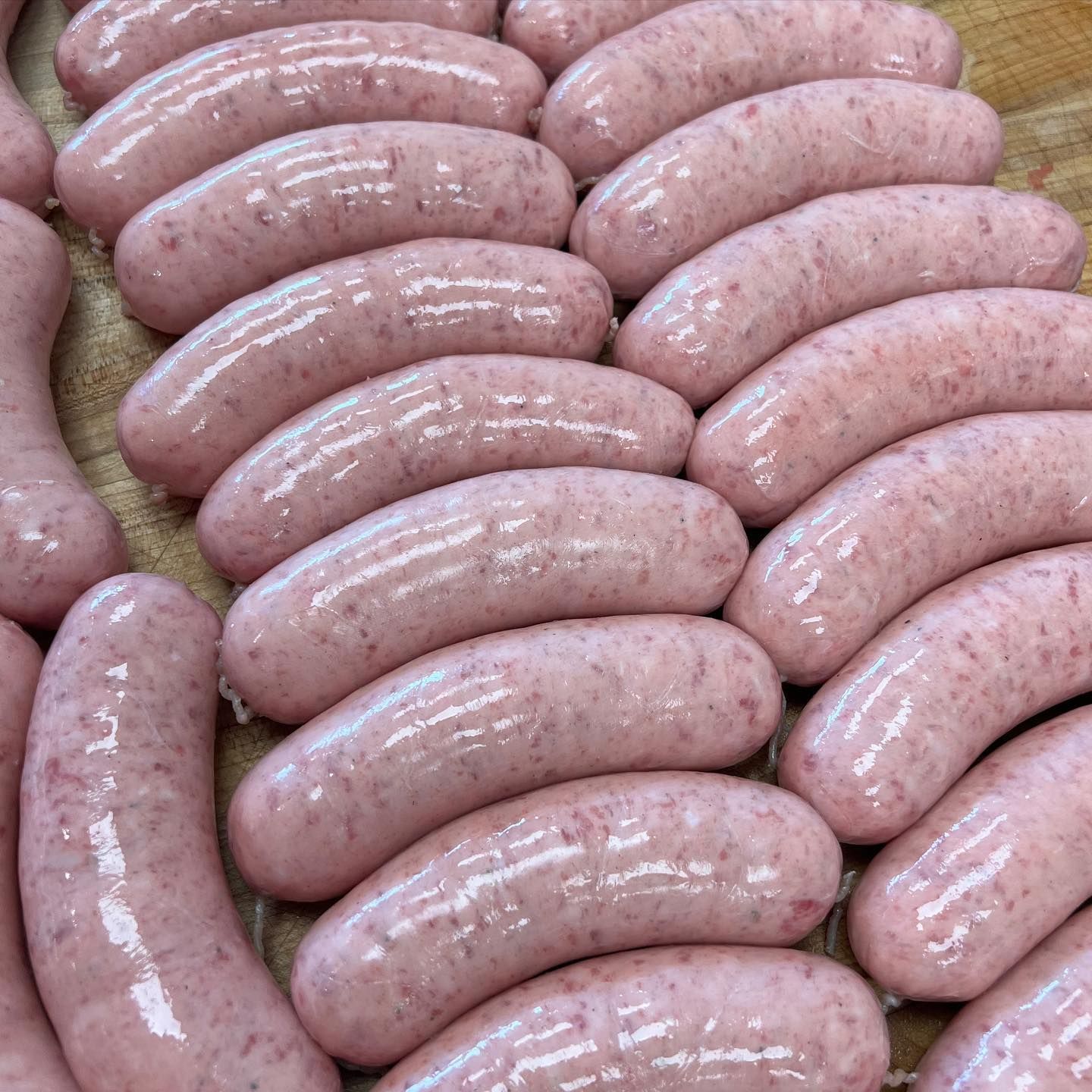 Rows of raw, pink sausages arranged on a wooden surface.