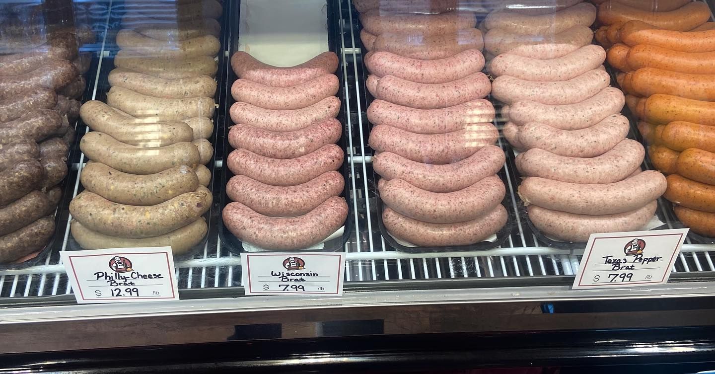 Sausages in a refrigerated display case with price labels. Ranging in color from light to dark, stacked in rows.