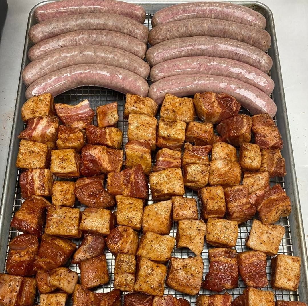 Raw sausages and seasoned pork belly cubes on a metal tray, ready for cooking.
