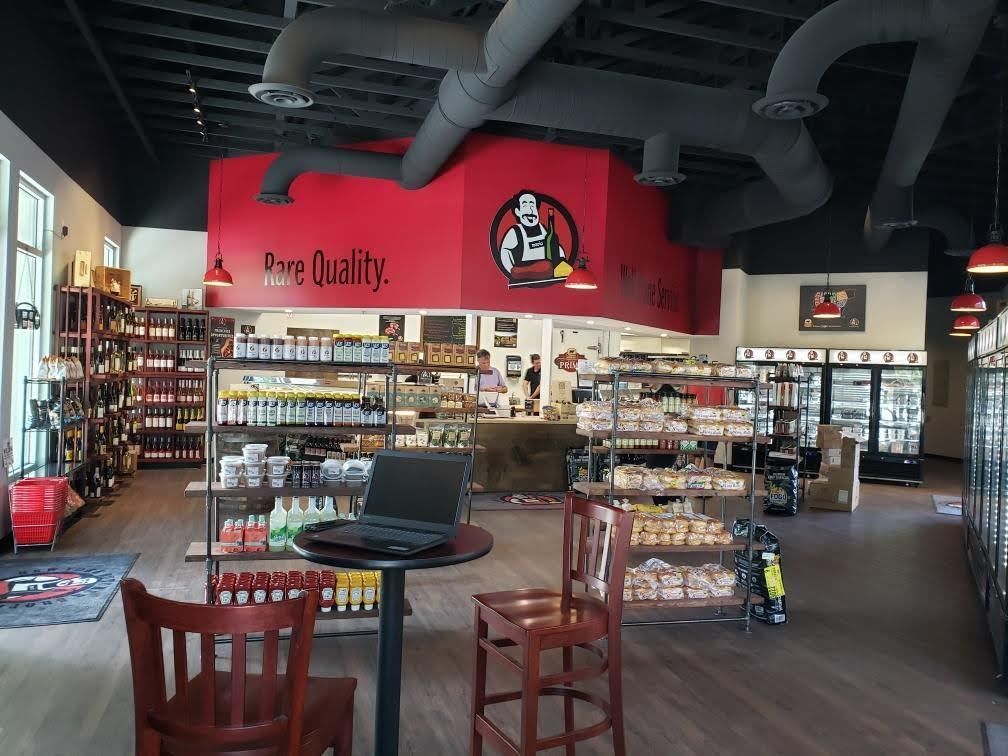 Interior of a grocery store with red accents and products on shelves. A laptop sits on a table with chairs.