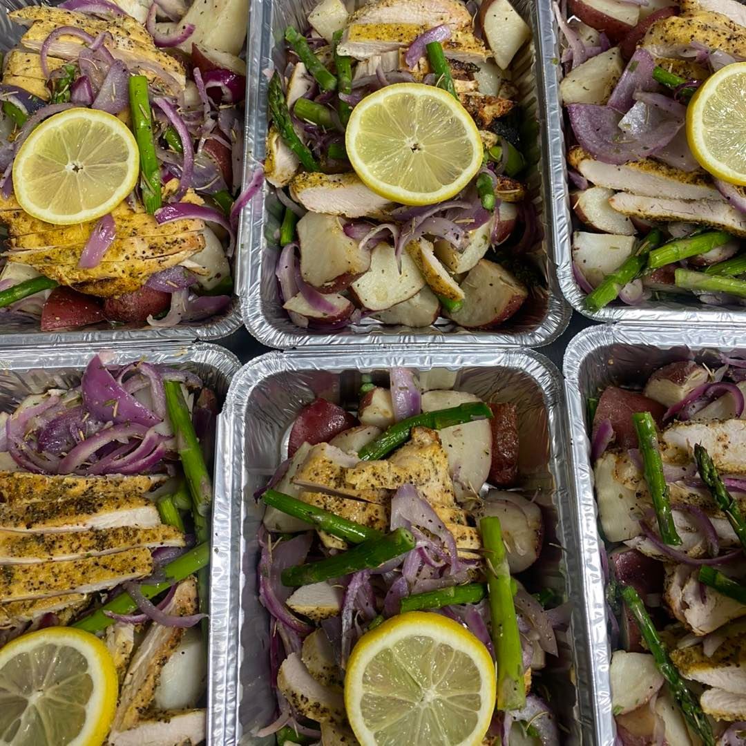 Six meal prep containers with chicken, red potatoes, asparagus, red onion, and lemon slices.