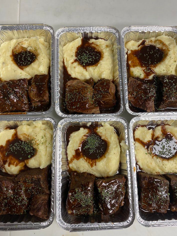 Six aluminum containers of short ribs with mashed potatoes and gravy.
