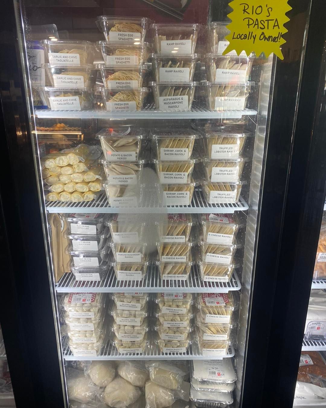 Refrigerator display of pre-packaged pasta dishes and dough balls.