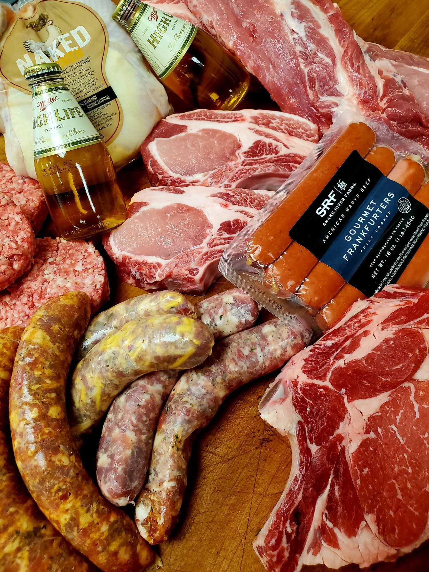 Assortment of raw meats, including pork chops, sausages, burgers, and steak, with bottles of beer.
