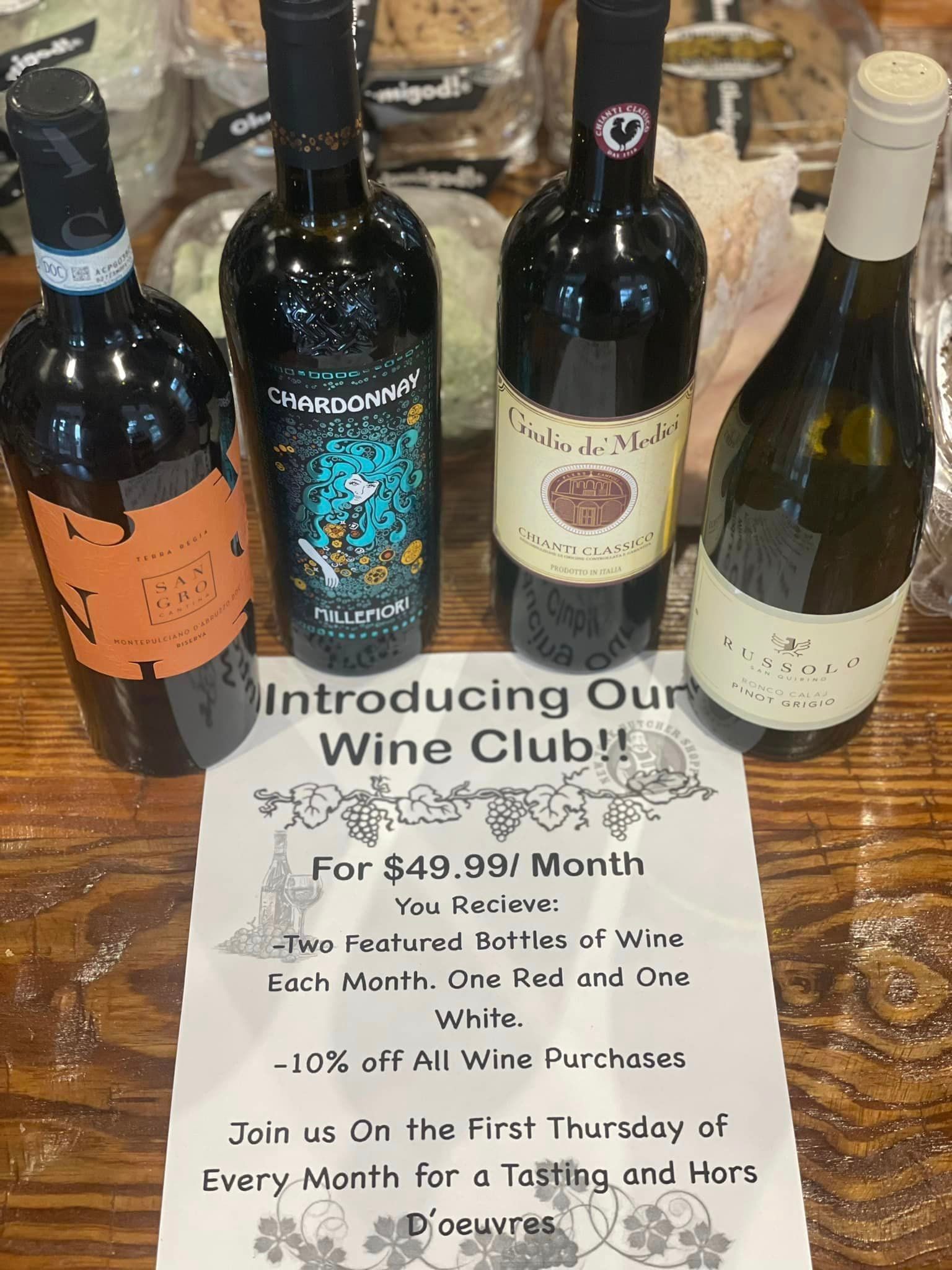 Four wine bottles and a promotional flyer for a wine club on a wooden surface.
