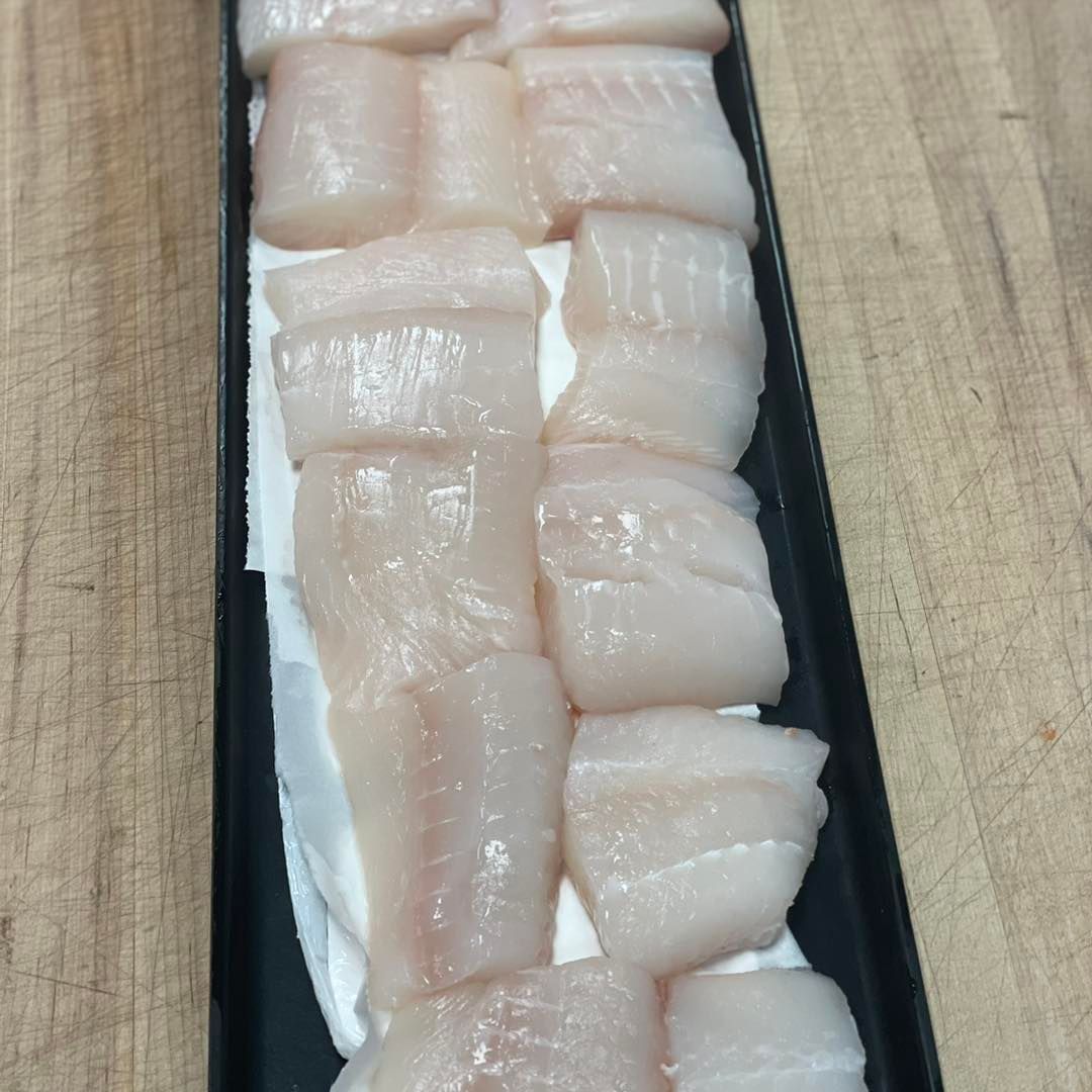 Raw, white fish fillets arranged in a black tray on a wooden surface.
