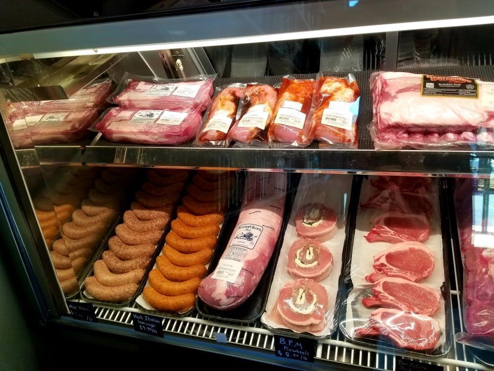 Meat display case with various cuts of pork: ribs, sausage, and chops.