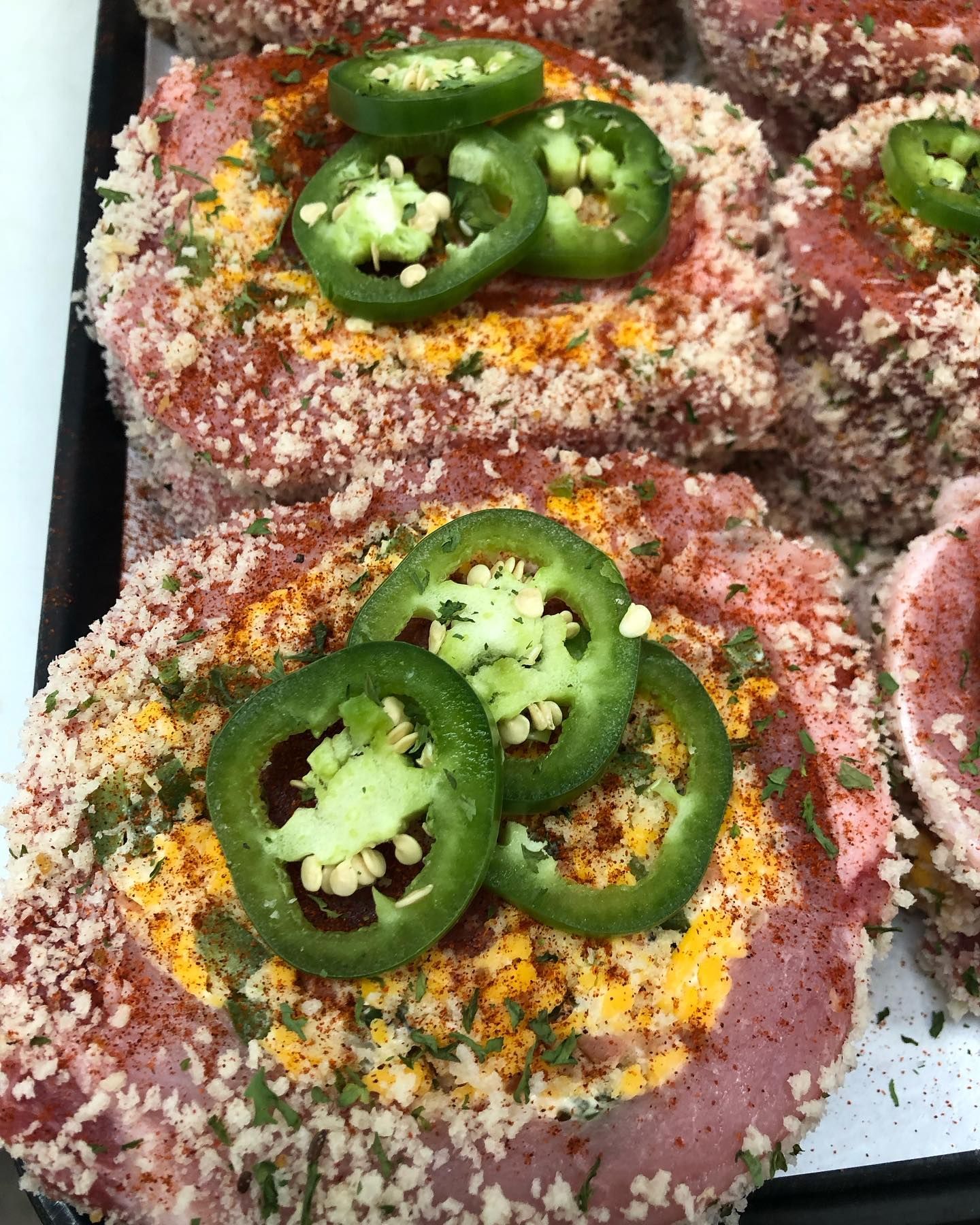 Breaded pork chops topped with jalapeño slices, seasoned with herbs and spices, on a tray.