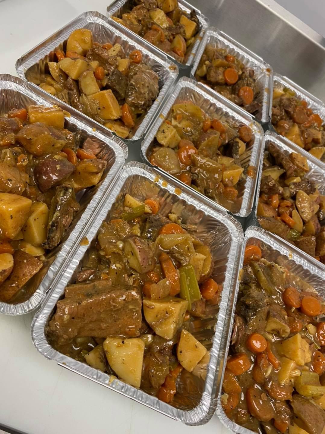 Individual aluminum foil trays filled with beef stew: potatoes, carrots, and meat.