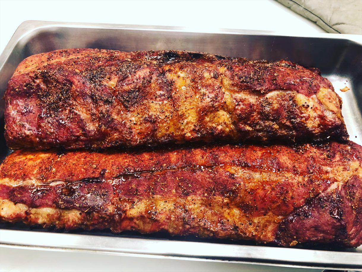 Two seasoned pork belly slabs in a metal pan, reddish-brown with spice rub.
