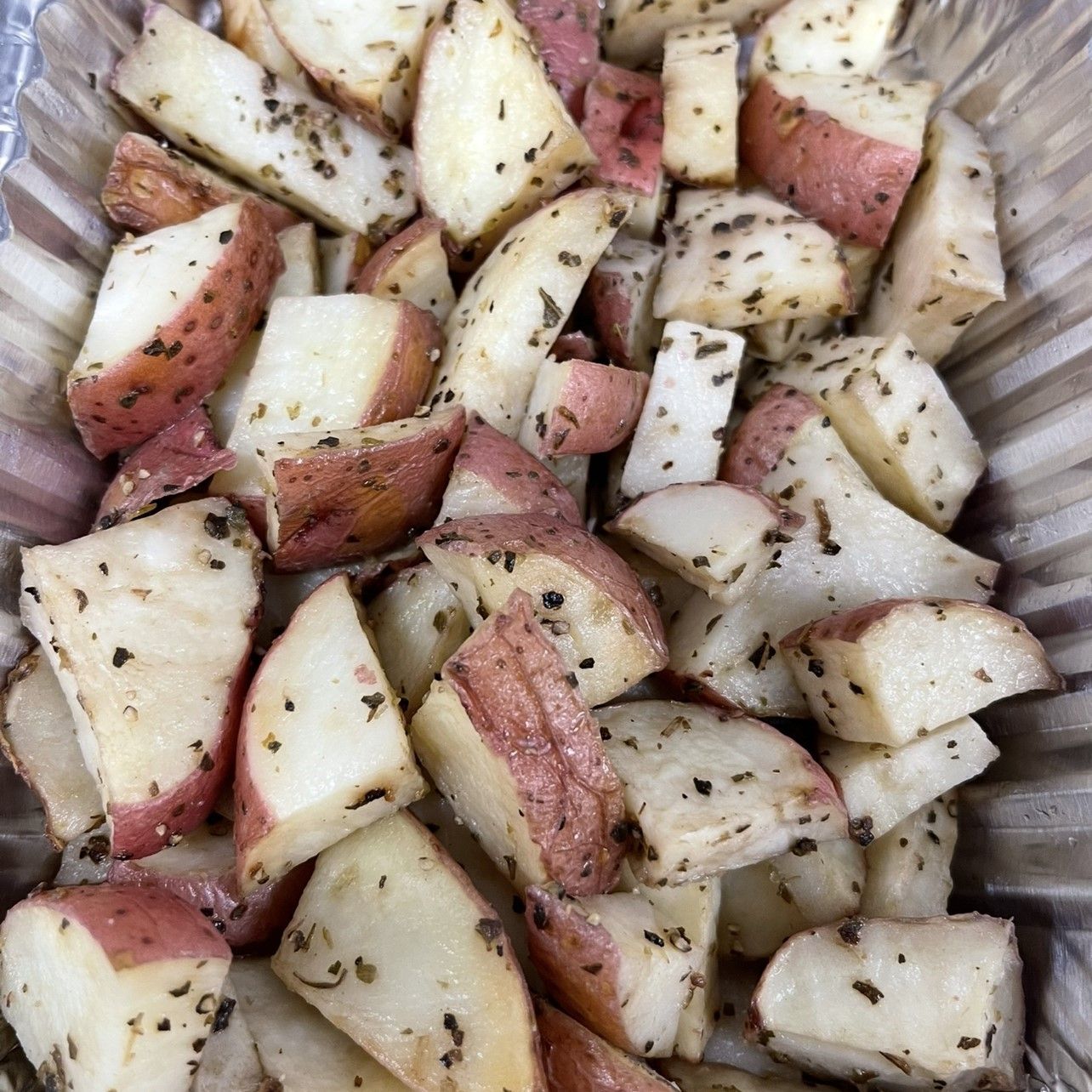 Roasted red potatoes, cut into chunks, seasoned with herbs in a metal container.