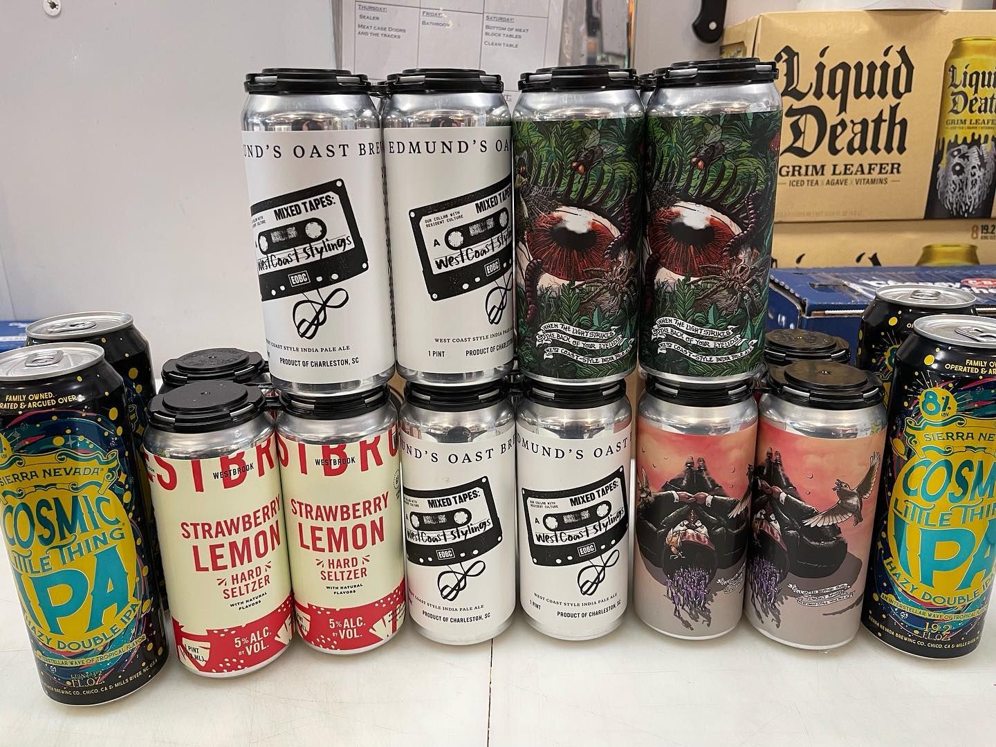 Assortment of beer cans featuring diverse designs, including cassette tapes and colorful art, arranged on a shelf.