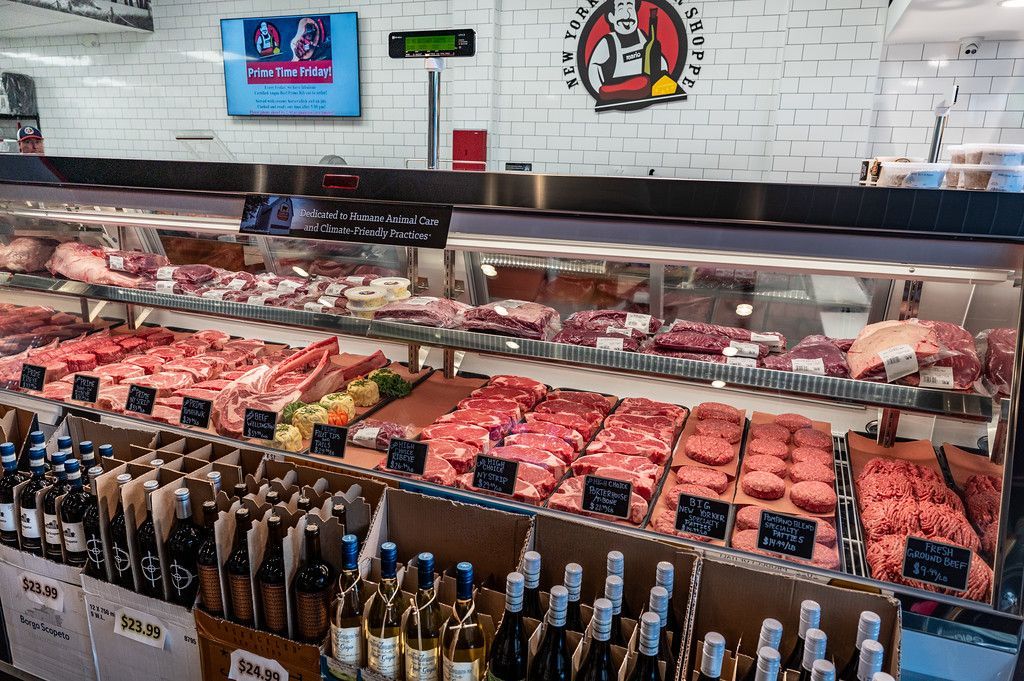 Meat display case in a butcher shop, showcasing various cuts of raw meat and bottles of wine.