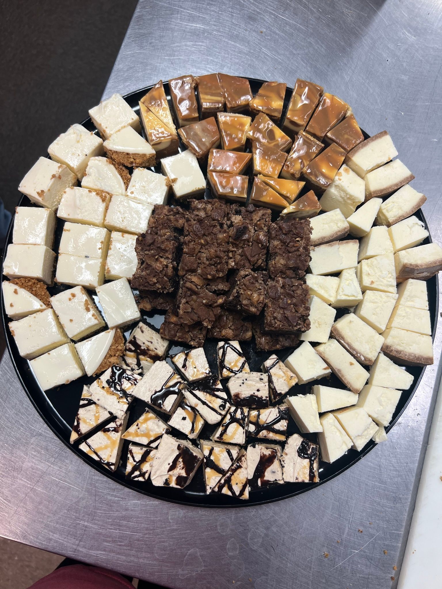Dessert tray with squares of cheesecake, caramel, fudge, and other treats.