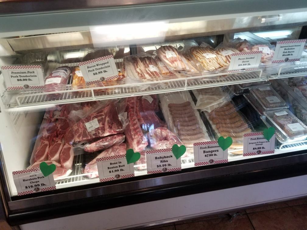 Display case filled with packaged cuts of meat, including bacon and pork chops, at a butcher shop.