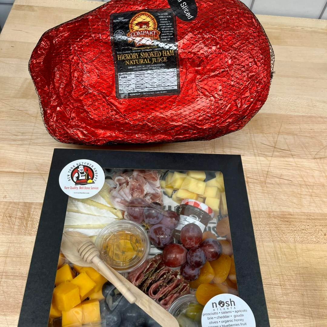 Whole, wrapped ham next to a charcuterie board with various foods.