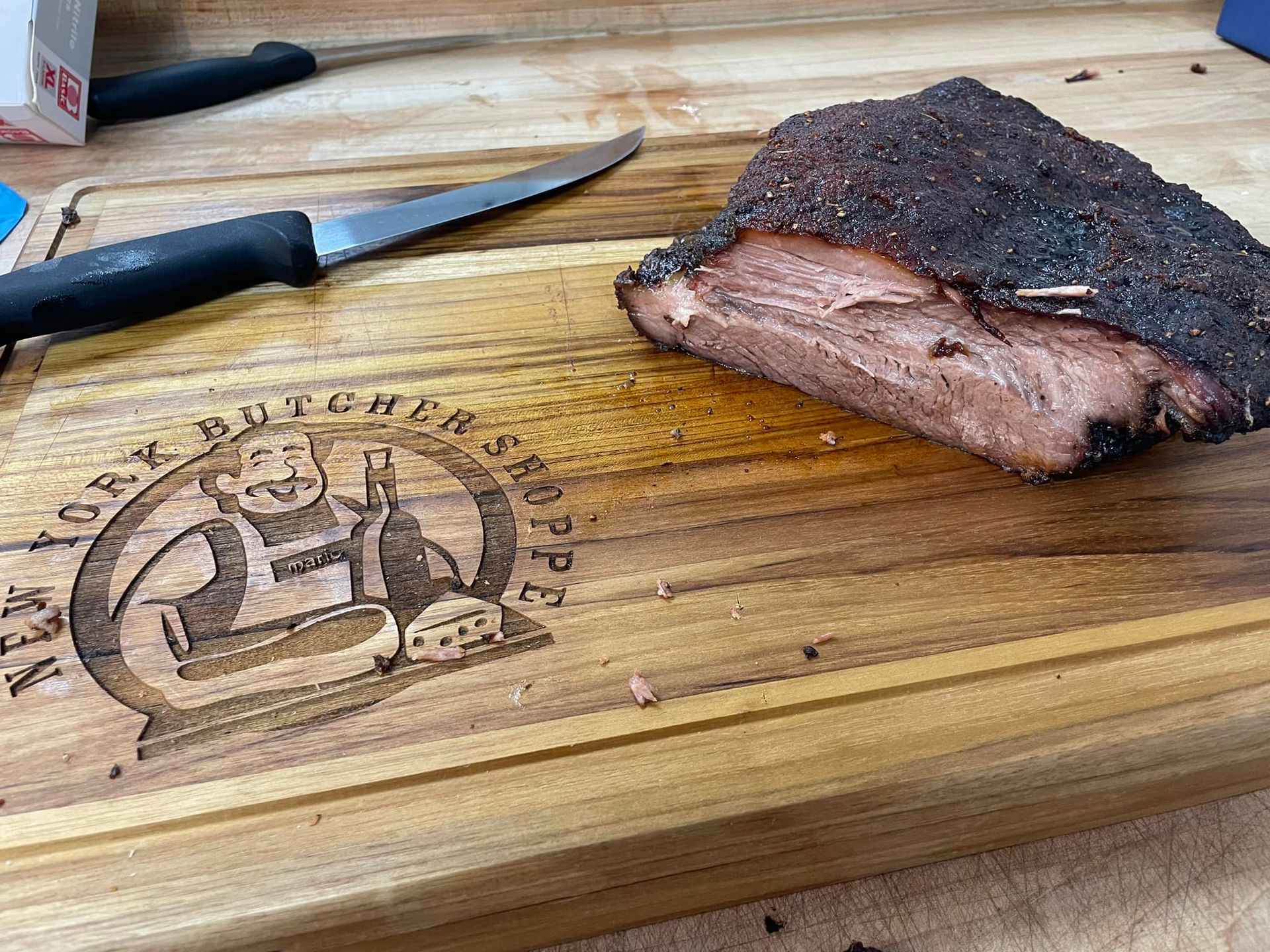 Smoked brisket on a wooden cutting board with a knife. The board has a butcher shop logo.