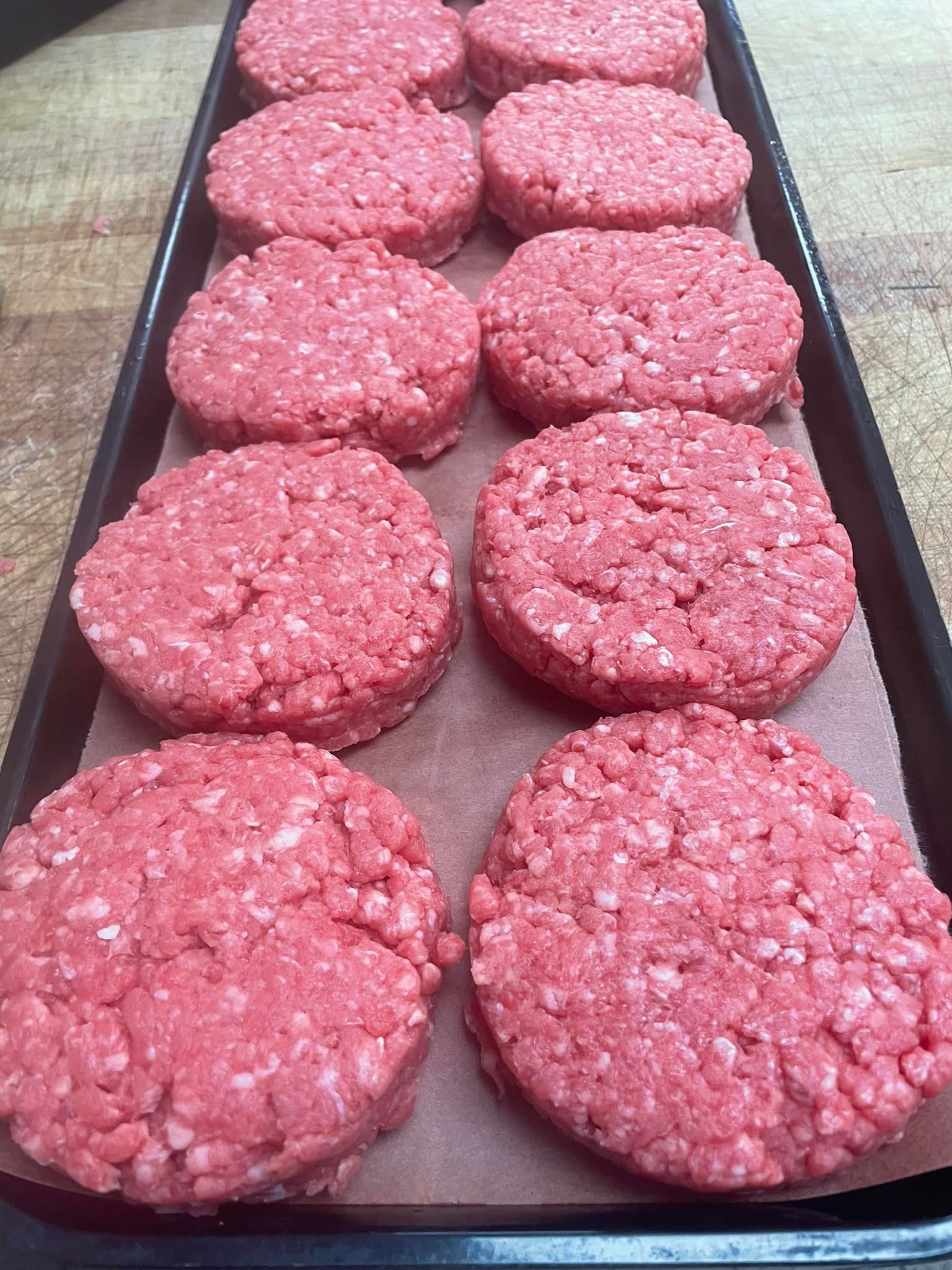Raw hamburger patties arranged in rows on a baking sheet.