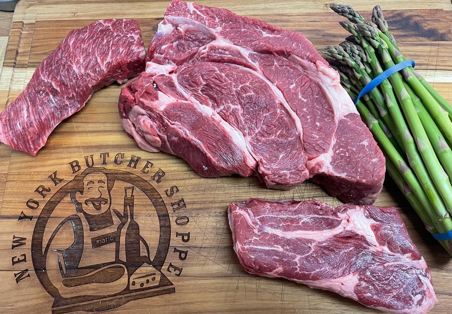 Raw steaks and asparagus on a butcher block, with a shop logo.