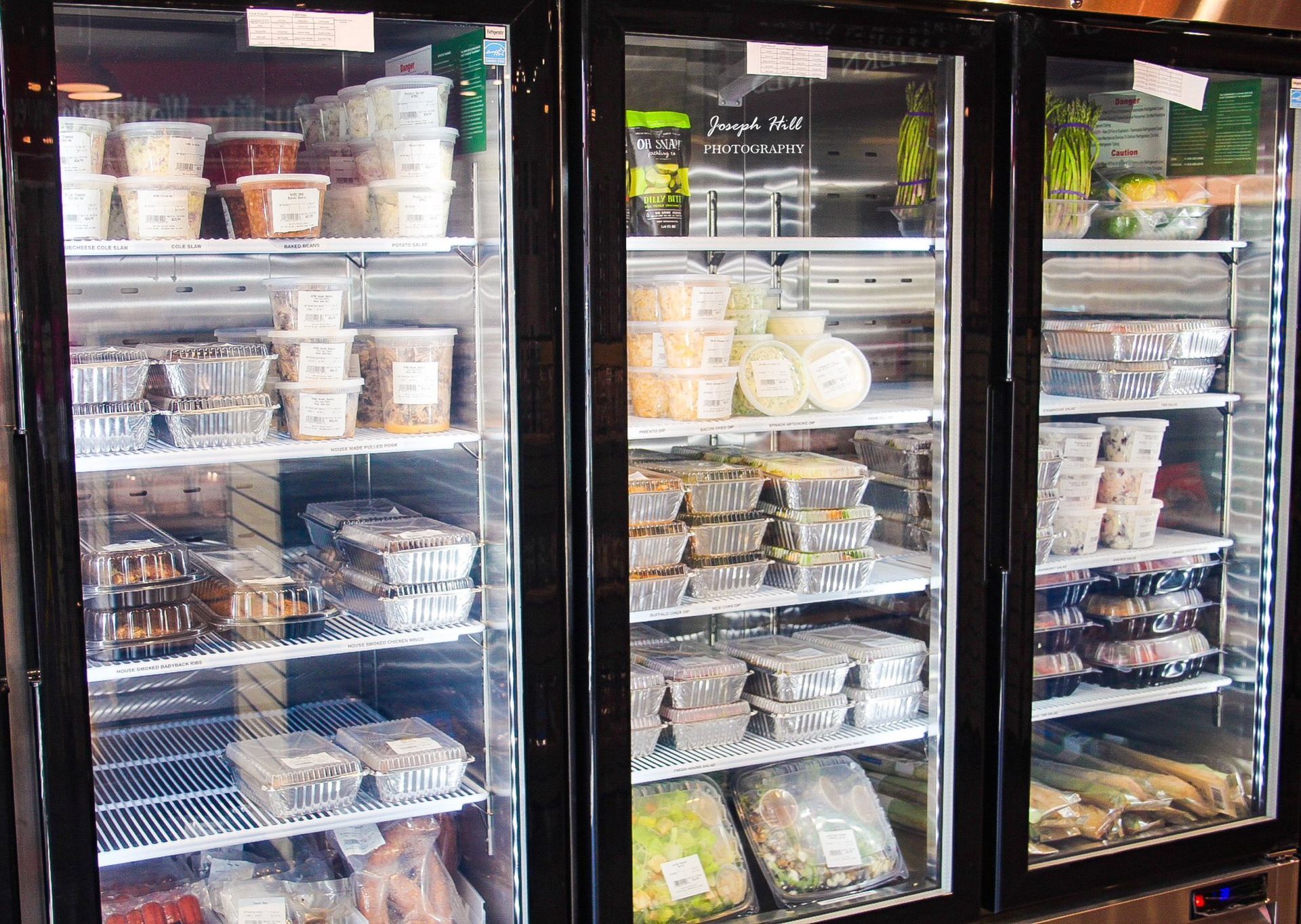 Three refrigerators display pre-made food containers and packaged items in a store.