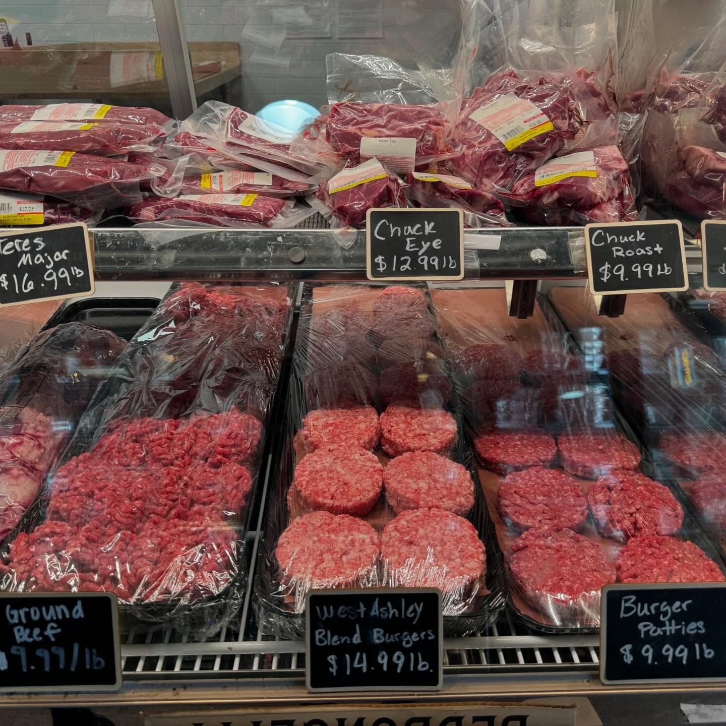 Meat display case with various cuts of beef, including ground beef and burger patties, labeled with prices.